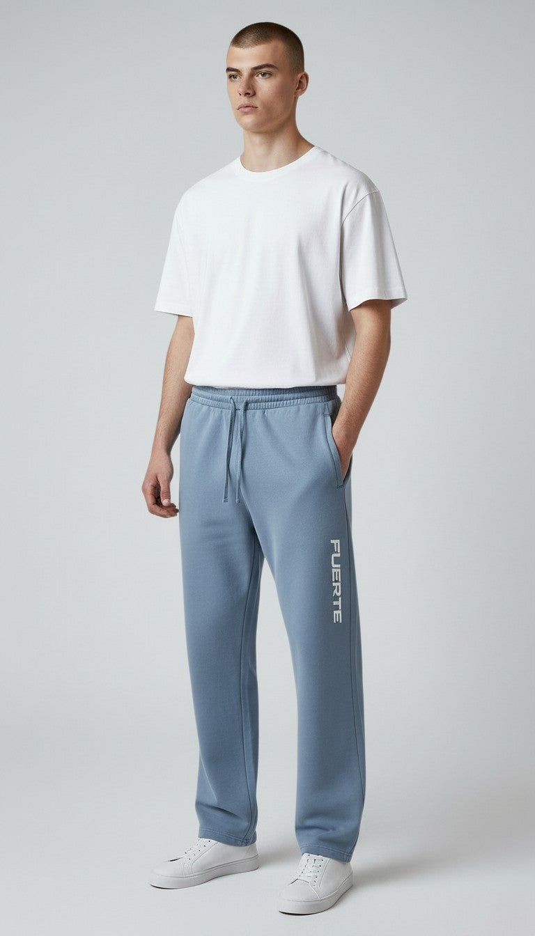Modell bär blå FUERTE vintage-tvättade unisex-sweatpants i bomull med lös passform och logotyp på benet.